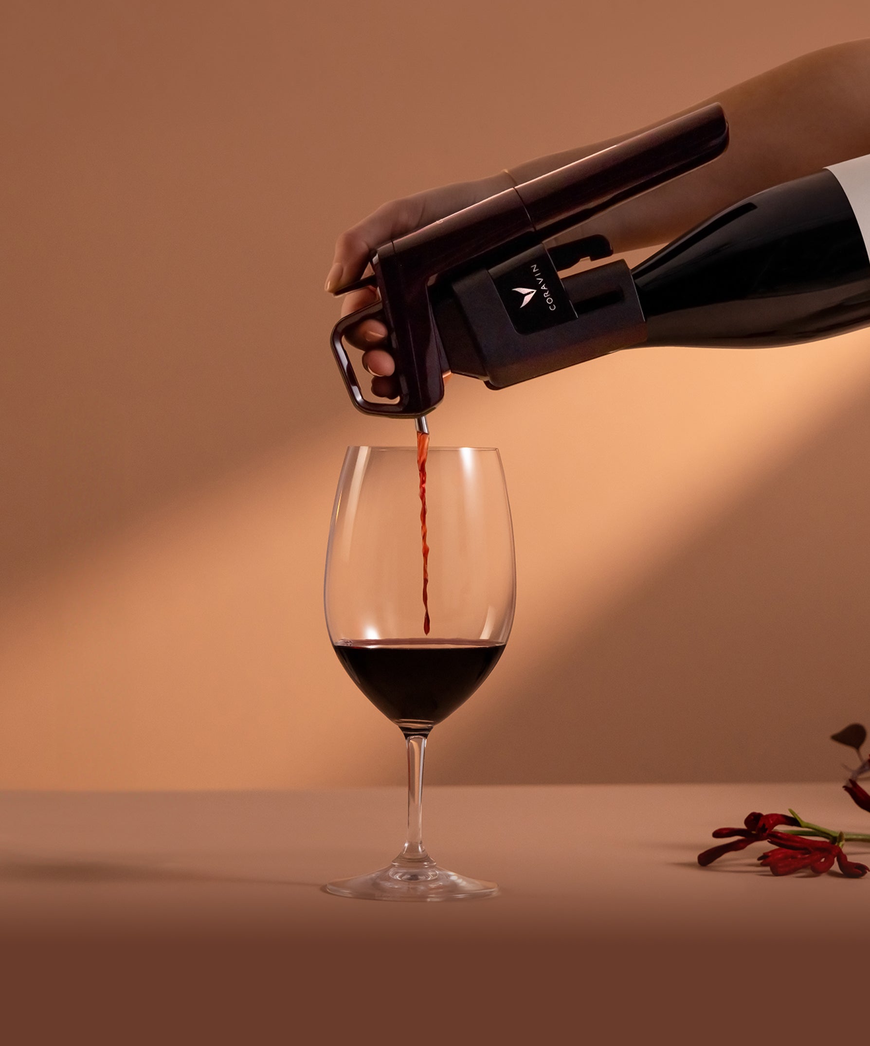 Person pouring red wine from a bottle into a glass with a neutral background